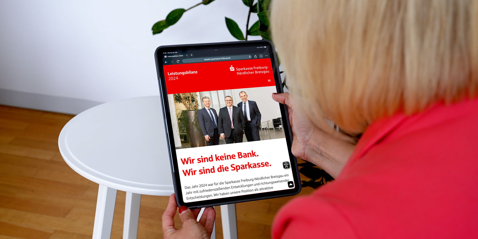 Frau betrachtet auf einem Tablet die digitale Leistungsbilanz 2024 der Sparkasse Freiburg-Nördlicher Breisgau mit dem Titel 'Wir sind keine Bank. Wir sind die Sparkasse.