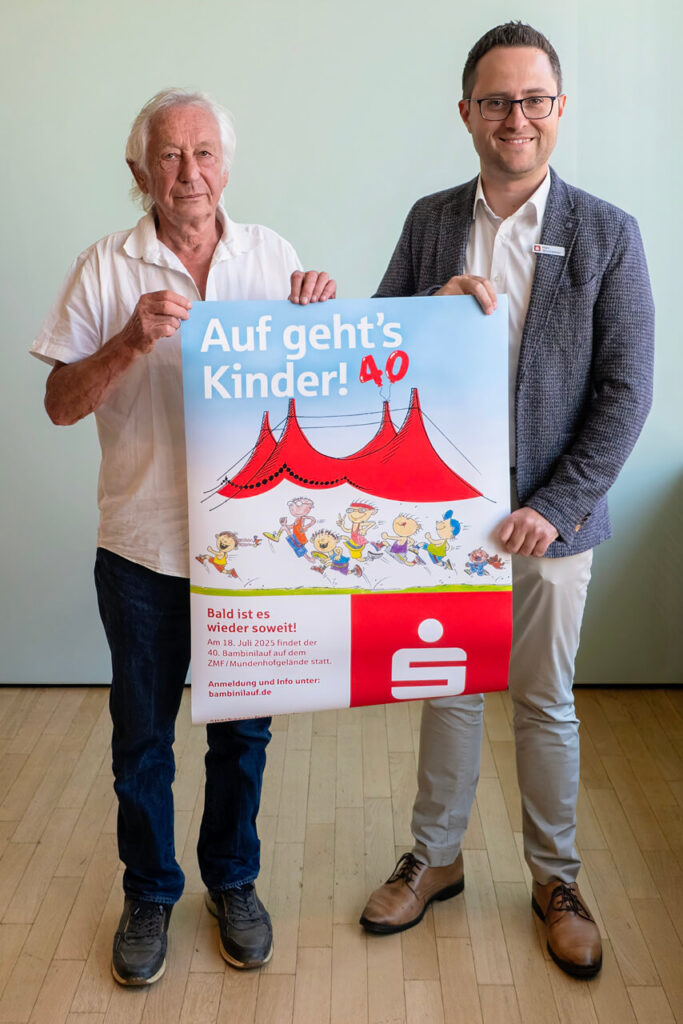 Albert Schultis und Marc Winsheimer halten ein Plakat zum 40. Bambinilauf der Sparkasse Freiburg-Nördlicher Breisgau.