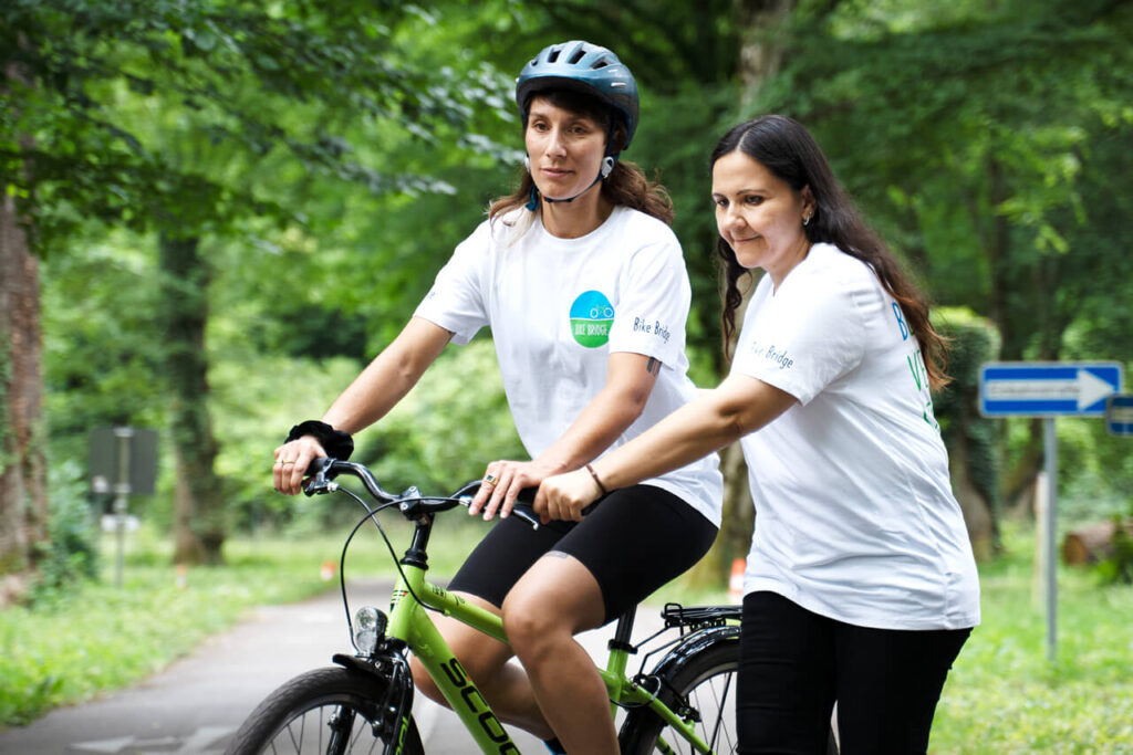 Yana Bergmann und Zeinab El Hage Ali beim Fahrradtraining im Rahmen des Projekt Bike & Belong – eine fährt, die andere unterstützt sie dabei.