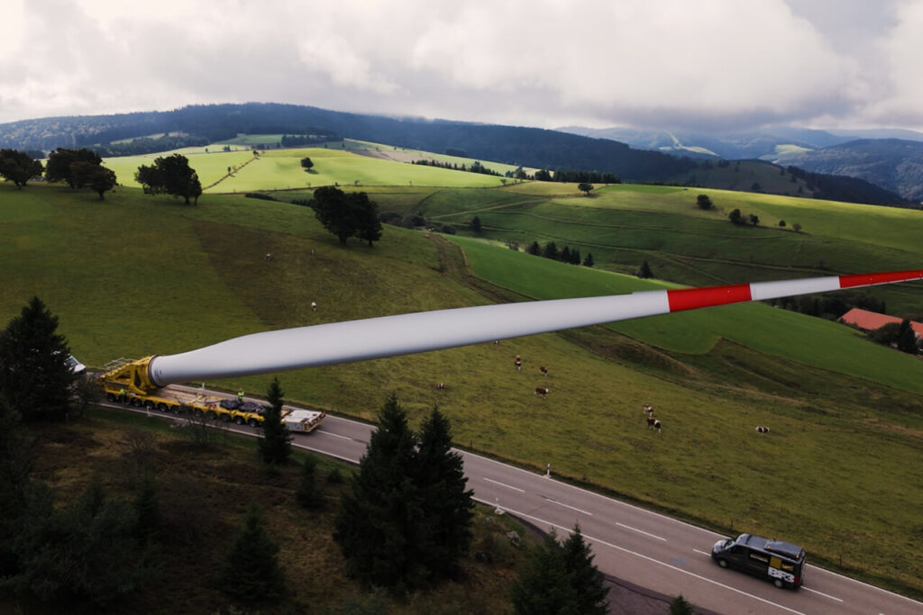 Transport eines Windradflügels durch den Schwarzwald, mit Blick über grüne Hügel und Weiden.