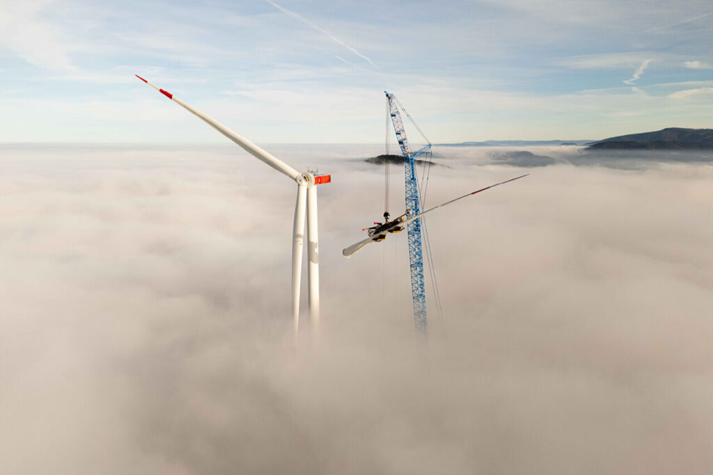 Montage eines Windradflügels am Taubenkopf im Schwarzwald, das Windrad ragt aus einer dichten Nebeldecke heraus.