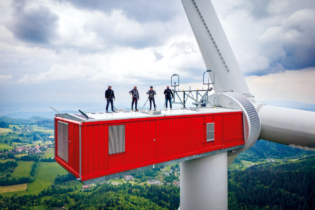 Vier Personen stehen auf dem Maschinenhaus eines Windrads auf dem Taubenkopf bei Freiburg im Schwarzwald.