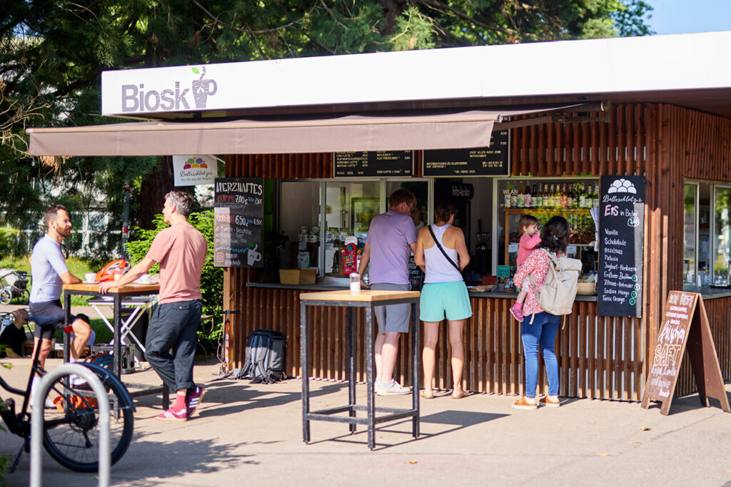 Menschen vor dem Freiburger Biosk im Grünen – mit Kind, Cappuccino und Radhelm.