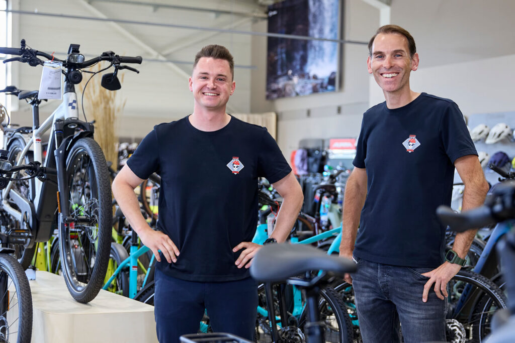 Sebastian Meyer und Jan Hättich von HOT.BIKE stehen lächelnd zwischen Fahrrädern im Verkaufsraum der Filiale in Teningen.
