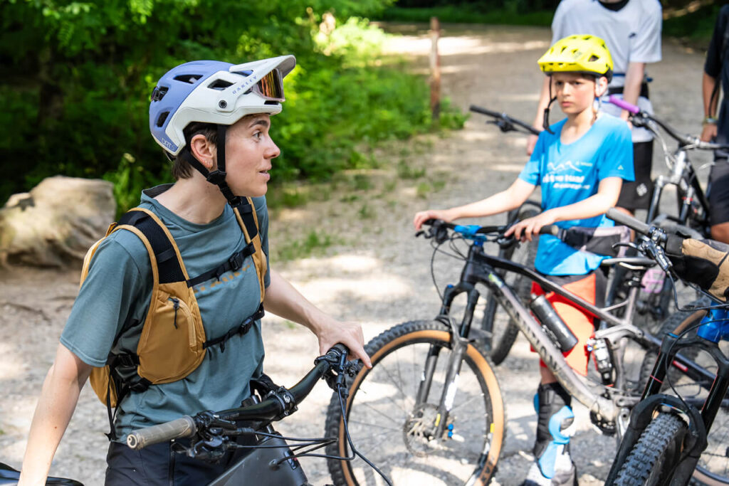 Lena Kehry erklärt beim Jugendtraining von Mountainbike Freiburg e. V. eine Übung – mit dabei Kinder mit Helm und Mountainbike.