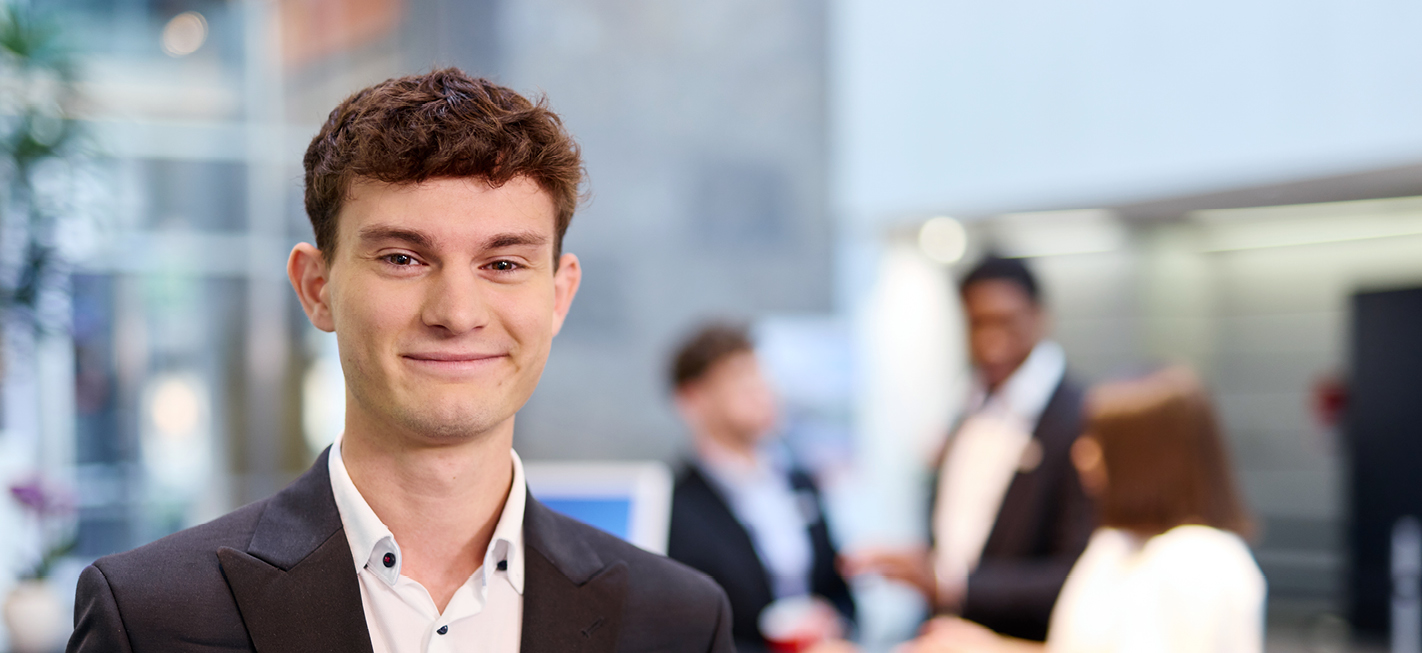 Dualer Student Manuel im FinanzZentrum Freiburg, im Vordergrund, unscharfe Personen im Hintergrund.“