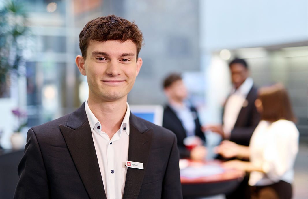 Dualer Student Manuel im FinanzZentrum Freiburg, im Vordergrund, unscharfe Personen im Hintergrund.“