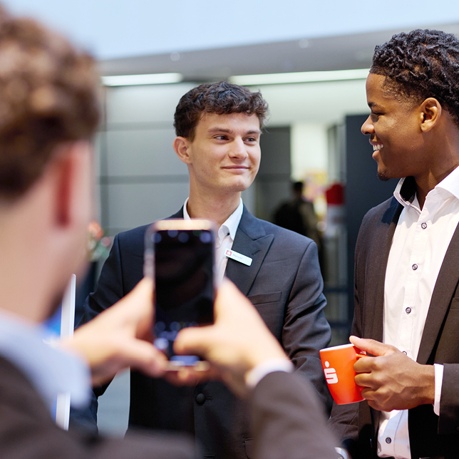 Azubi Jonas fotografiert seine Kollegen Manuel und Joys beim Gespräch im Sparkassen-FinanzZentrum.