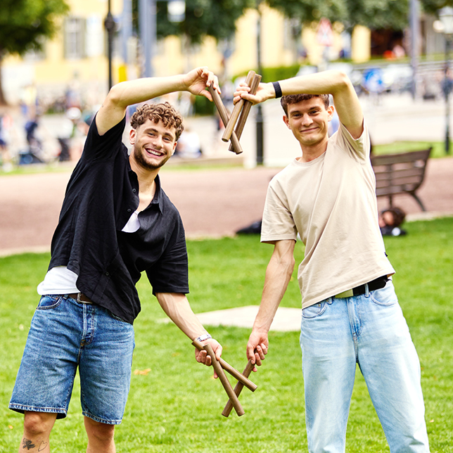 Azubis Jonas und Manuel formen mit Schwedenschach-Stäben und Armen gemeinsam ein Herz.