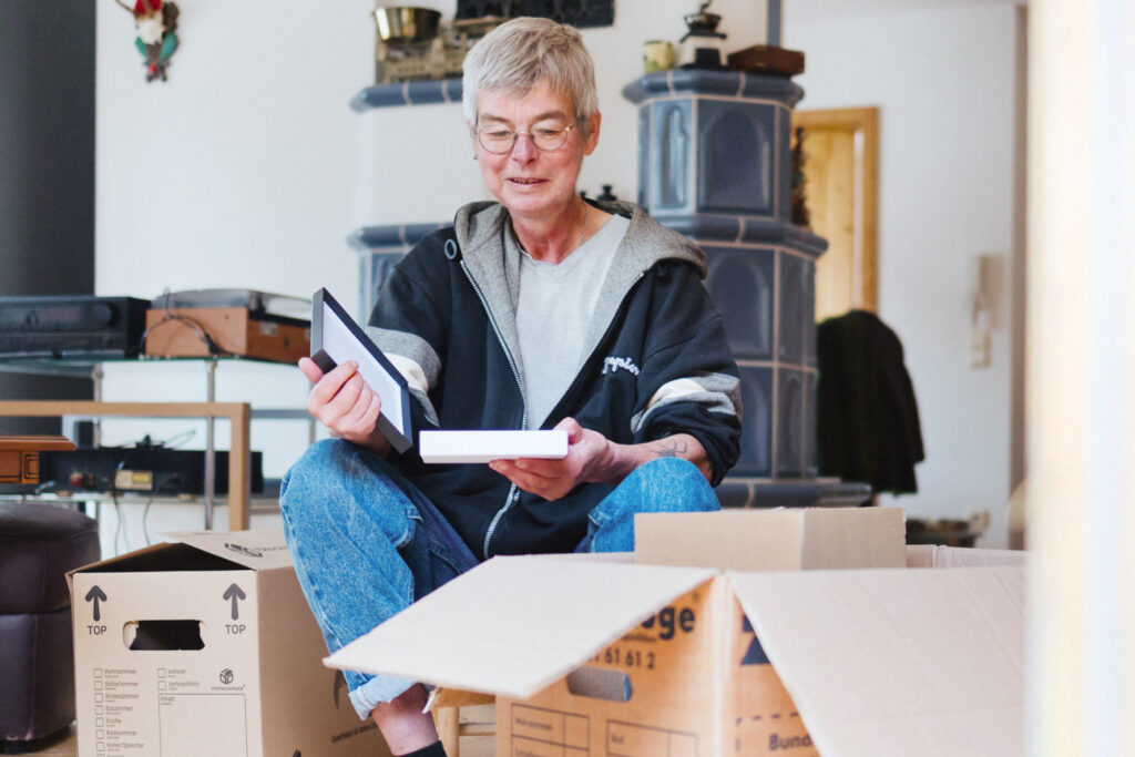 Frau mit Brille sitzt zwischen Umzugskartons und hält einen Bilderrahmen in der Hand