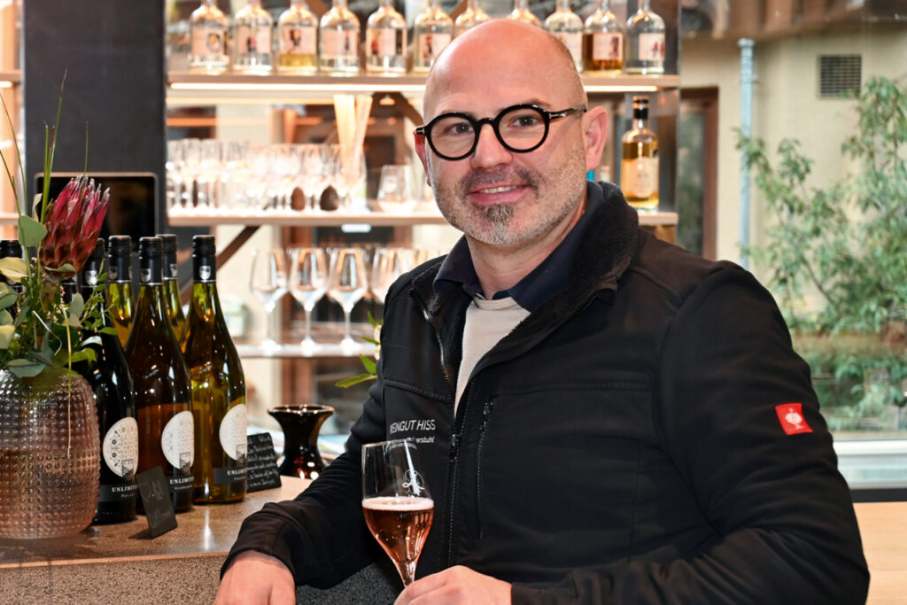 Porträt von Andreas Hiss vom Weinhaus Hiss in Eichstetten an einer Bar mit Weinflaschen und gefülltem Glas.