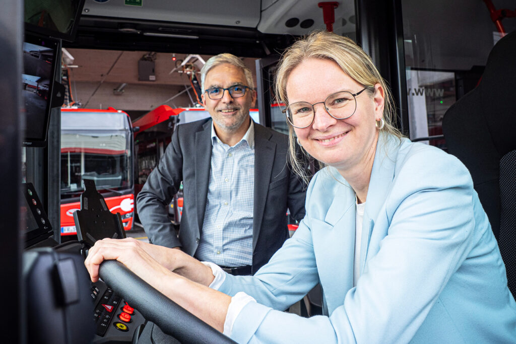 Mareike Rehl und Uwe Schlupf sitzen in einem Bus auf dem VAG Betriebshof, im Hintergrund sind weitere Fahrzeuge zu sehen.