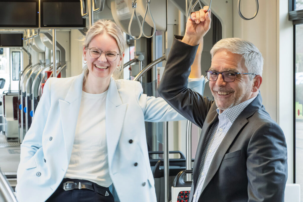 Mareike Rehl und Uwe Schlupf stehen lächelnd im Innenraum einer Straßenbahn und halten sich an einer Halteschlaufe fest.