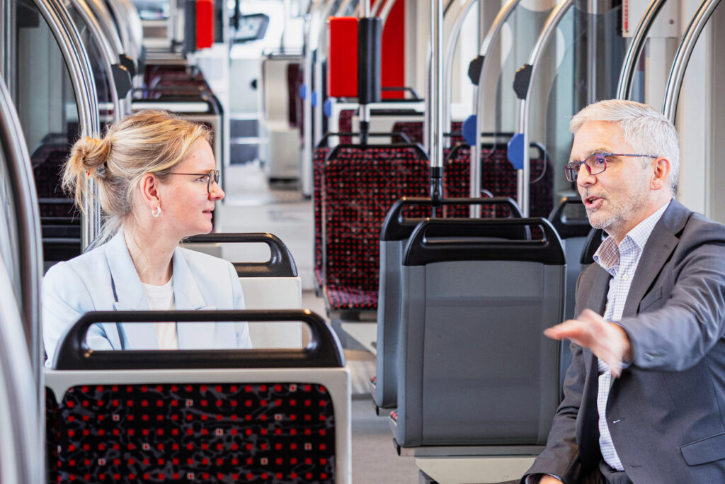 Mareike Rehl und Uwe Schlupf sitzen im Innenraum einer Straßenbahn und sprechen miteinander.