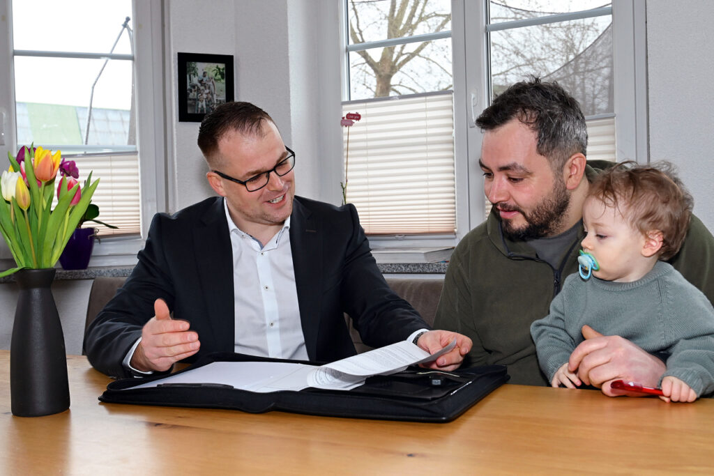 Florian Ruf bespricht mit Ralf Stephan und dessen Sohn Theo Unterlagen an einem Tisch im Wohnraum.