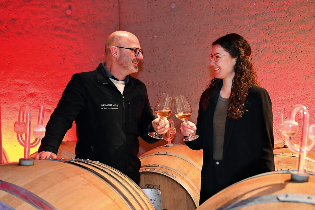 Andreas Hiss und Lenja Kraft verkosten im Barrique Keller des Weinhauses Hiss ein Glas Wein zwischen Holzfässern.