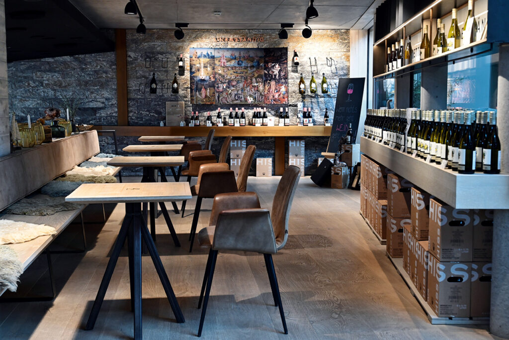 Innenraum des Weinhauses Hiss mit Sitzplätzen, Weinregalen und Verkaufsfläche.