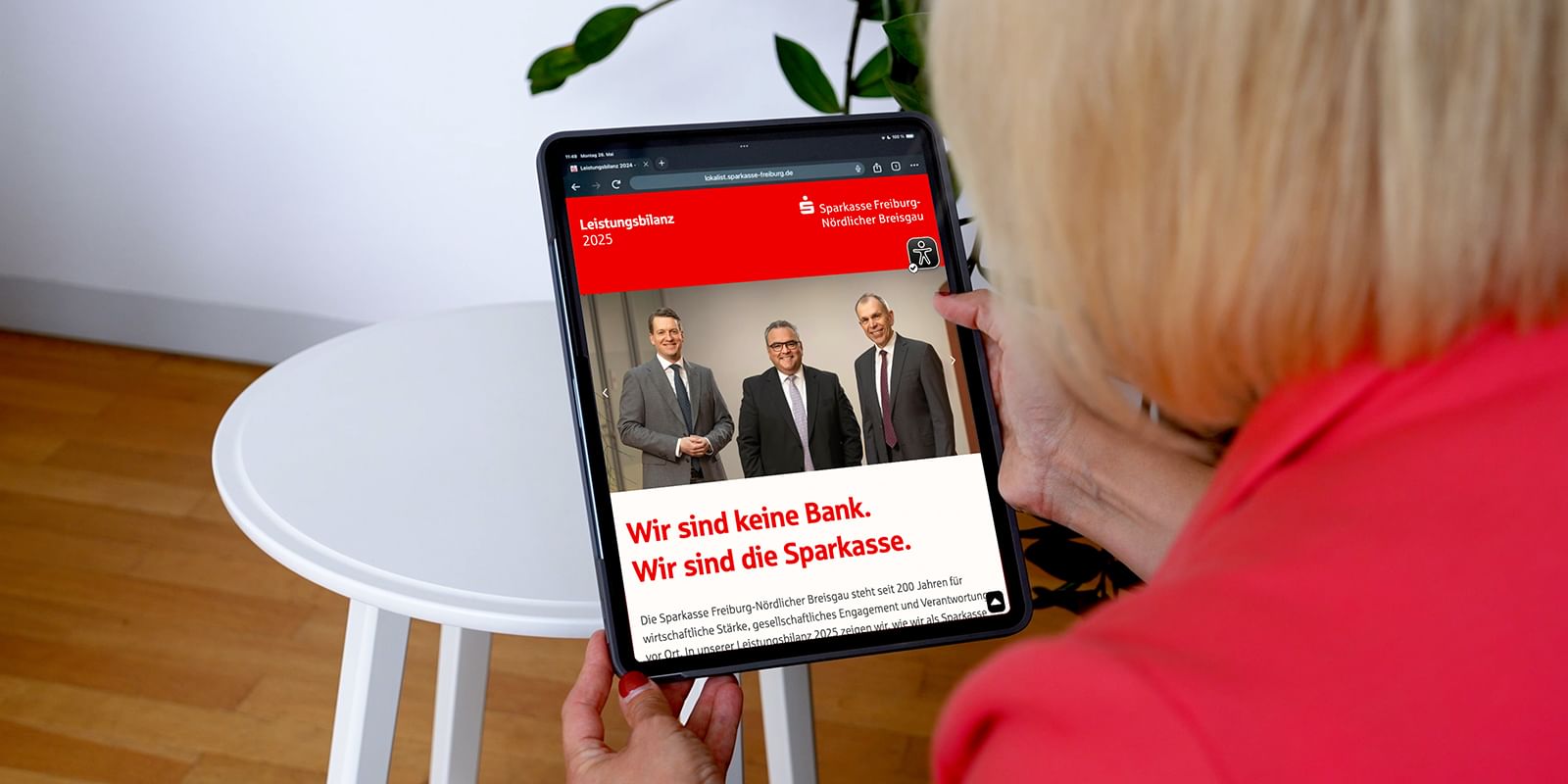 Frau betrachtet auf einem Tablet die digitale Leistungsbilanz 2024 der Sparkasse Freiburg-Nördlicher Breisgau mit dem Titel 'Wir sind keine Bank. Wir sind die Sparkasse.